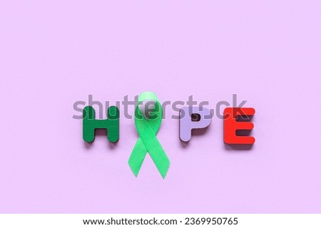 Green awareness ribbon and word HOPE made of wooden letters on purple background. Mental Health Day