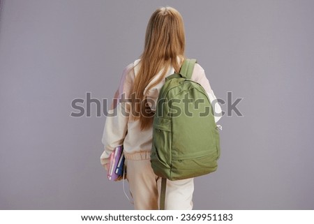Seen from behind young woman with backpack and workbooks isolated on grey. Royalty-Free Stock Photo #2369951183