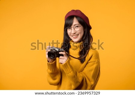 In her quest to capture life's beauty, young Asian woman, donning a yellow sweater and red beret, skillfully wields her camera as a talented photographer.