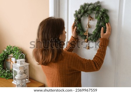 Beautiful young woman hanging beautiful Christmas wreath on door