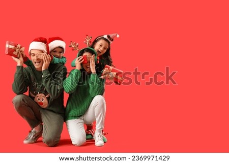 Little children surprising their parents with Christmas presents on red background Royalty-Free Stock Photo #2369971429