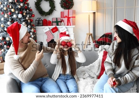 Little girl with Christmas balls and her parents at home