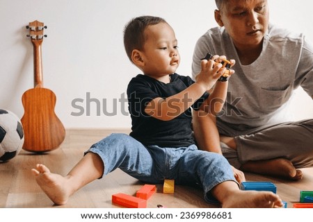 Happy Asian father and little son playing with colorful building blocks and toy cars at home