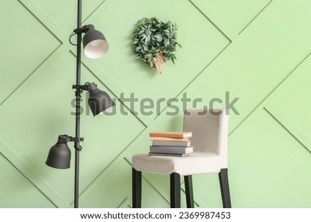 Chair with books, lamp and Christmas mistletoe wreath on green wall