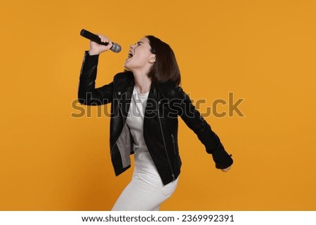 Beautiful young woman with microphone singing on yellow background
