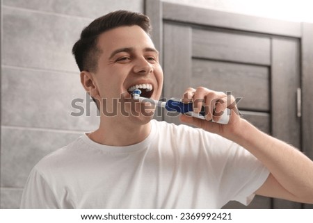 Man brushing his teeth with electric toothbrush in bathroom Royalty-Free Stock Photo #2369992421