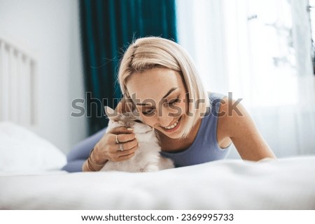 A beautiful, light-haired woman pets her cat on the bed in the bedroom