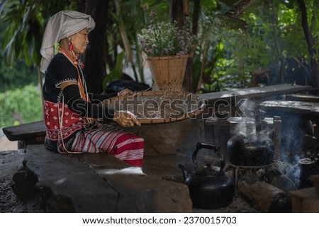 Karen hill tribe woman sorting coffee grounds in an old-style way with an old bamboo tray and dressed in traditional clothes at Doi Inthanon National Park a travel attraction in Chiang Mai, Thailand. Royalty-Free Stock Photo #2370015703