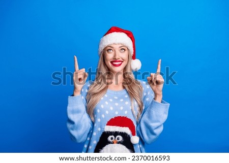 Photo portrait of lovely blonde young lady pointing up look empty space wear penguin sweater x-mas hat isolated on blue color background