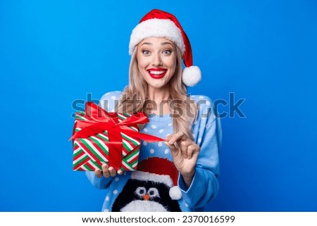 Photo portrait of lovely blonde young lady open present box pull ribbon wear penguin sweater x-mas hat isolated on blue color background Royalty-Free Stock Photo #2370016599