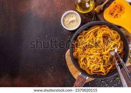 Homemade autumn pumpkin spaghetti pasta, vegan mediterranean, american vegan warming food with cheesy pumpkin sauce, garlic and thyme, dark concrete background top view copy space