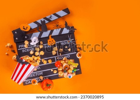 Horror movie, series night, Halloween cinema party with trick-or-treating sweets bucket, popcorn, movie clapperboard and Halloween decorations on high-colored background copy space