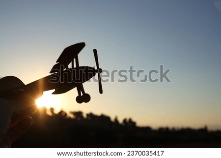 close up photo of man's hand holding toy airplane against sunset sky