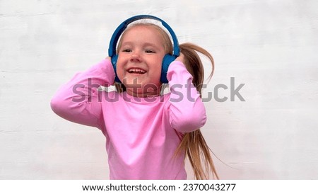 A little girl with a charming smile listens to music in wireless headphones and dances. Positive emotions of the child. on a white background