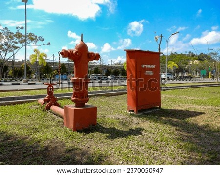 Red fire hydrant in the park for emergency fire access.
Text in picture "perhatian" means "attention" and "area parkir kendaraan khusus bus" means "special parking area for buses".