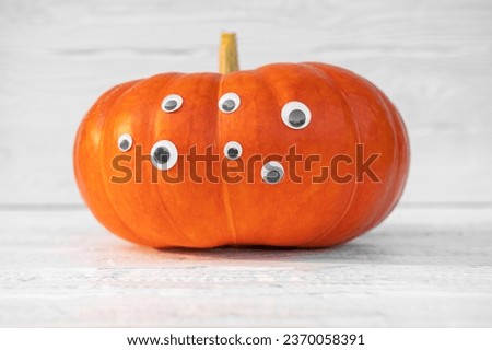 Pumpkin with Eyes for Halloween. Humor, Creative. One Big Orange Pumpkin with Many Eyes. Single Spooky Halloween Pumpkin, Jack O Lantern with Evil Face. White Wooden Textured Background. Front View