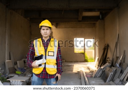 Young Asian engineer inspects architecture, construction project concept, young professional engineer in helmet and blueprint paper at house construction site.