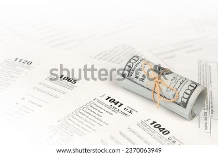 Tax forms lies near roll of hundred dollar bills. Income tax return. Time to pay taxes concept. 1040 1041 1120 and 1065 empty blank forms Royalty-Free Stock Photo #2370063949