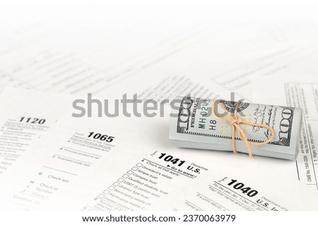 Tax forms lies near roll of hundred dollar bills. Income tax return. Time to pay taxes concept. 1040 1041 1120 and 1065 empty blank forms Royalty-Free Stock Photo #2370063979