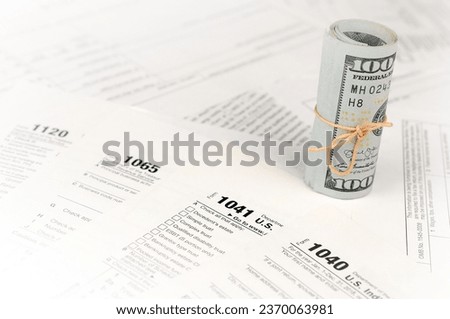 Tax forms lies near roll of hundred dollar bills. Income tax return. Time to pay taxes concept. 1040 1041 1120 and 1065 empty blank forms Royalty-Free Stock Photo #2370063981