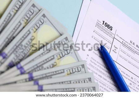 1065 tax form lies near hundred dollar bills and blue pen on a light blue background. US Return for parentship income. Royalty-Free Stock Photo #2370064027