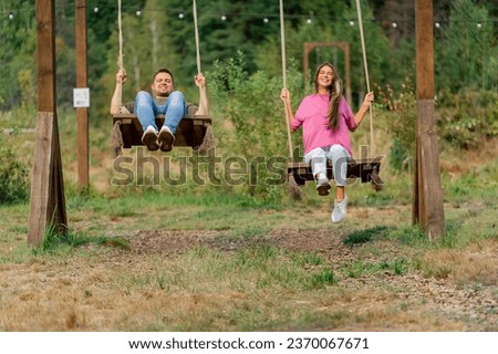 Loving couple man and girl riding on a large wooden swing overlooking a beautiful lake in nature Royalty-Free Stock Photo #2370067671