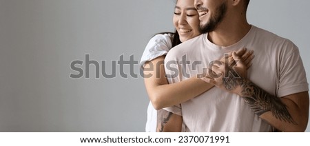 Joyful asian woman hugging tattooed husband with closed eyes isolated on grey, banner shot	