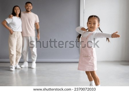 Smiling asian child dancing near blurred parents on grey background	
