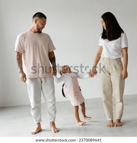 Smiling young asian parents holding hands of toddler daughter on grey background