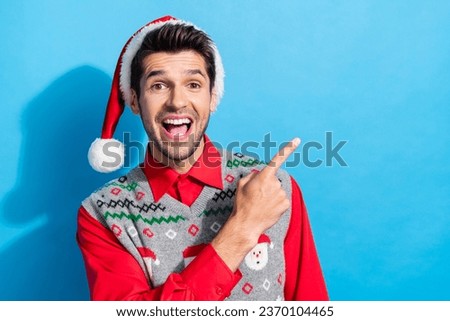 Photo portrait of nice young male excited point empty space dressed x-mas print vest hat garment isolated on blue color background