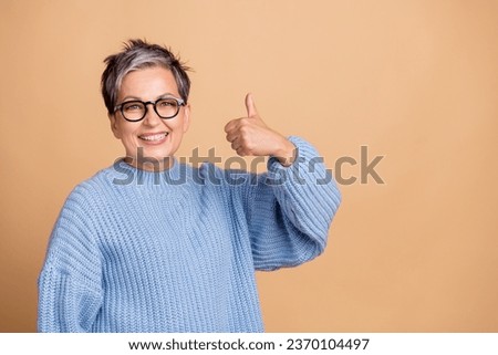 Photo portrait of lovely retired female showing thumb up wear trendy blue knitwear outfit isolated on beige color background
