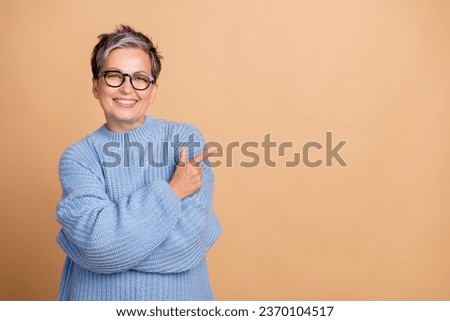 Photo portrait of lovely retired female finger point empty space dressed stylish blue knitted outfit isolated on beige color background