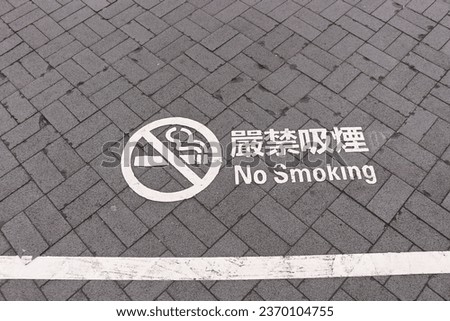 No smoking sign painted in white colour on grey bricks pavement. Chinese words written "no smoking".