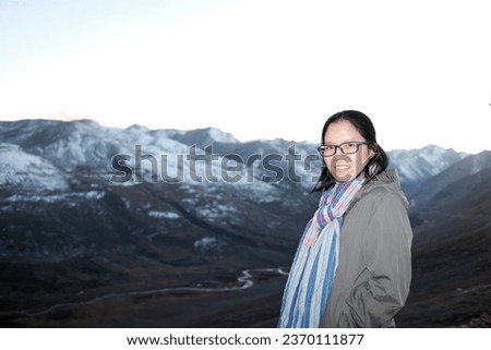 An Asian female tourist is posing with view of the snow capped mountains at Chilas Pass on Karakoram highway, Pakistan during the sunset.