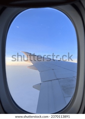 View from an airplane’s window during a soft sun rise with a thick carpet of clouds. An airplane wing occupies half of the picture.