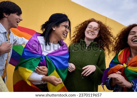 Group excited young diverse people laughing yellow wall background. LGBT community enjoying gay pride day outdoors. Liberal people celebrating street party. Rainbow flags and friends of generation z. Royalty-Free Stock Photo #2370119657