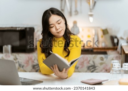Beautiful Asian woman smiling happily relaxing using laptop technology Take notes Drink a relaxing hot drink while sitting on the table in your room at home.