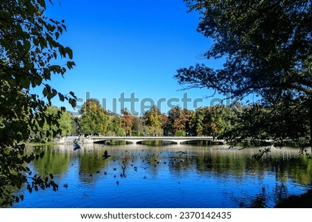 Landscape with long old grey bridge and many large green trees near the lake in Carol Park in Bucharest, Romania,  in a sunny autumn day