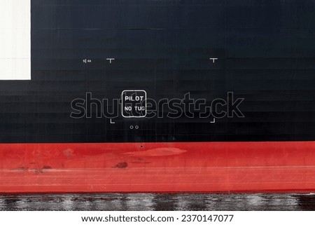 Section of the black and red hull of a ship with letters PILOT No Tug 