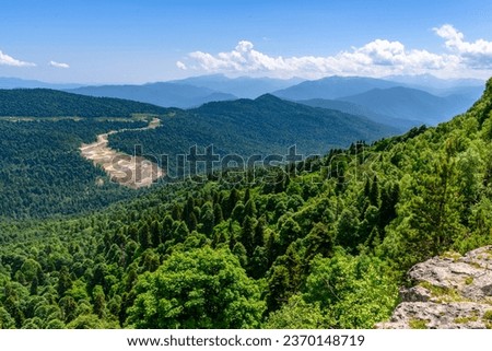 Scenic panoramic view of idyllic rolling hills landscape with blooming meadows and snowcapped alpine mountain peaks. A beautiful sunny day with blue sky and clouds in springtime.