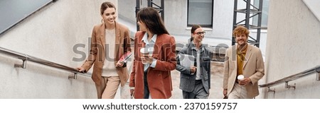 smiley coworkers in smart casual outfits walking upstairs looking at each other, coworking, banner Royalty-Free Stock Photo #2370159757