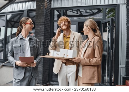 three young colleagues holding papers and scale model talking on mobile phone, design bureau