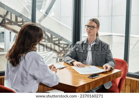 two young coworkers man and woman discussing their paperwork sitting at table, coworking concept
