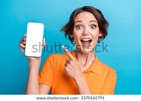 Photo of adorable excited lady wear orange t-shirt open mouth showing finger modern device empty space isolated blue color background