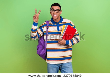 Photo portrait of handsome young guy college student showing v-sign wear trendy striped outfit isolated on green color background