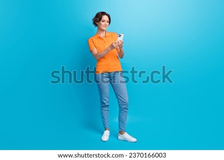 Full size photo of cheerful positive girl dressed stylish polo denim pants look at smartphone read post isolated on blue color background