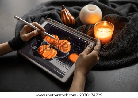 Girl's hands in special glove draw still life picture with pumpkins on electronic tablet near burning candle. The concept of inspiration, creativity, modern art. Halloween, Thanksgiving day