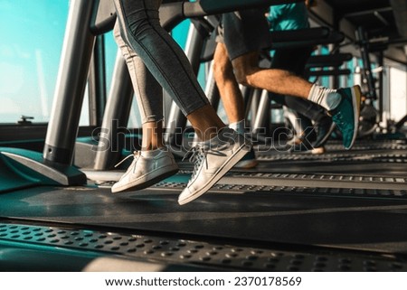 Picture of people wearing sports shoes running on treadmill in gym. Photo of people practicing cardio with only legs and feet in the frame.