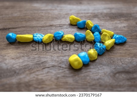 An arrow made of small stones. Wooden background. Colors of the Ukrainian flag. Movement symbol. Route direction. Two colors. Stone texture.