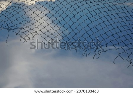 Looking up at a chain link fence with blue sky and clouds. wire fence. Chain link fence see sky. Opening in metallic fence. blue sky. Challenge. breakthrough concept.                            